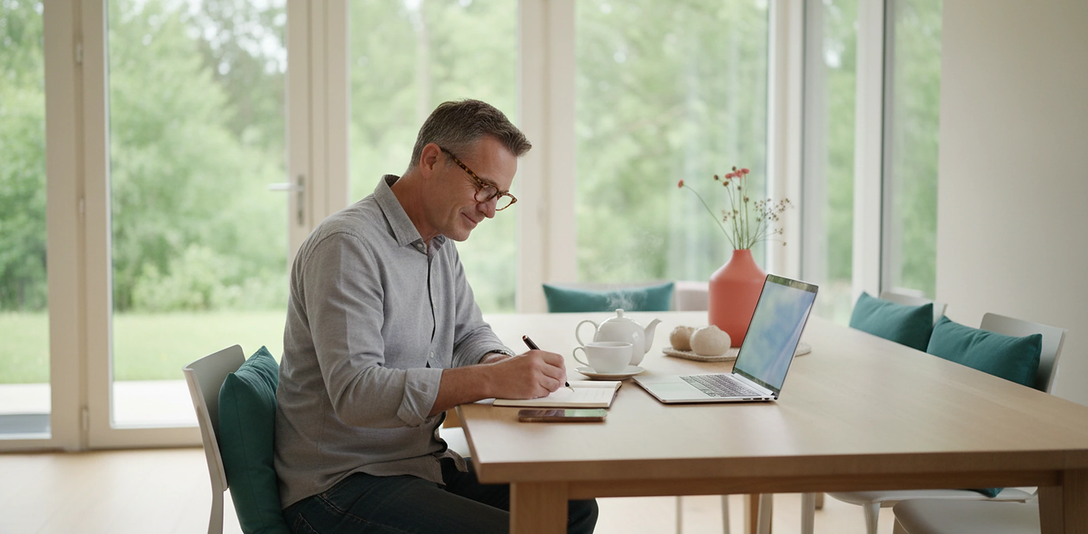 Man writing notes for his grant application next to a laptop